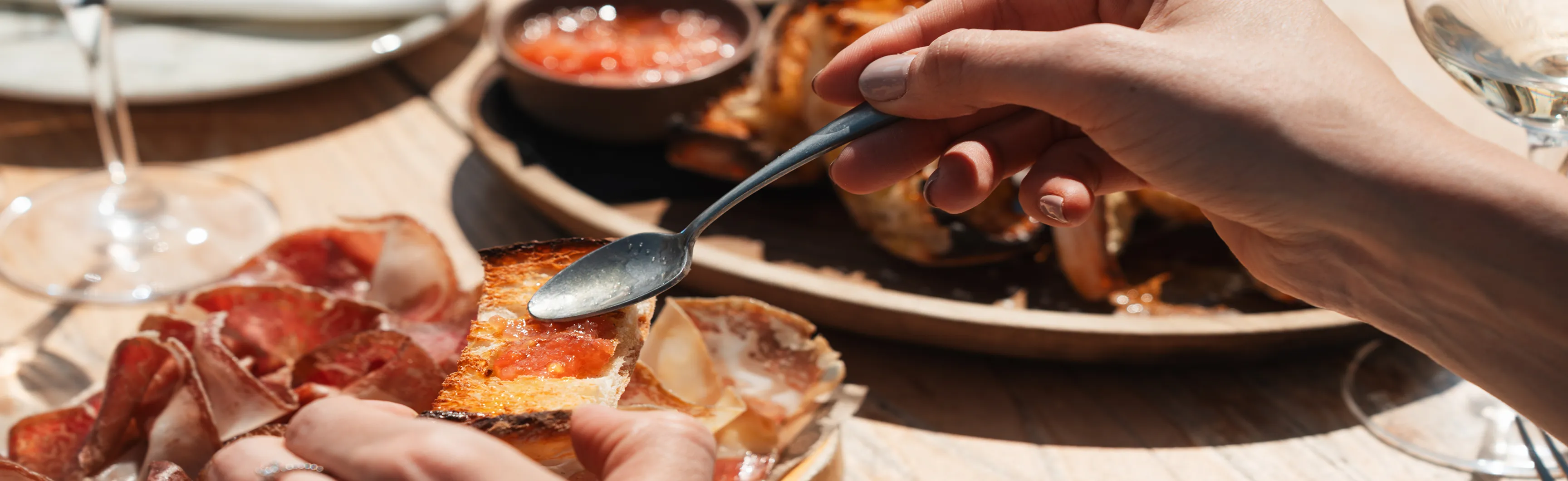Närbild på hand som breder pålägg på bröd, i bakgrunden tapas